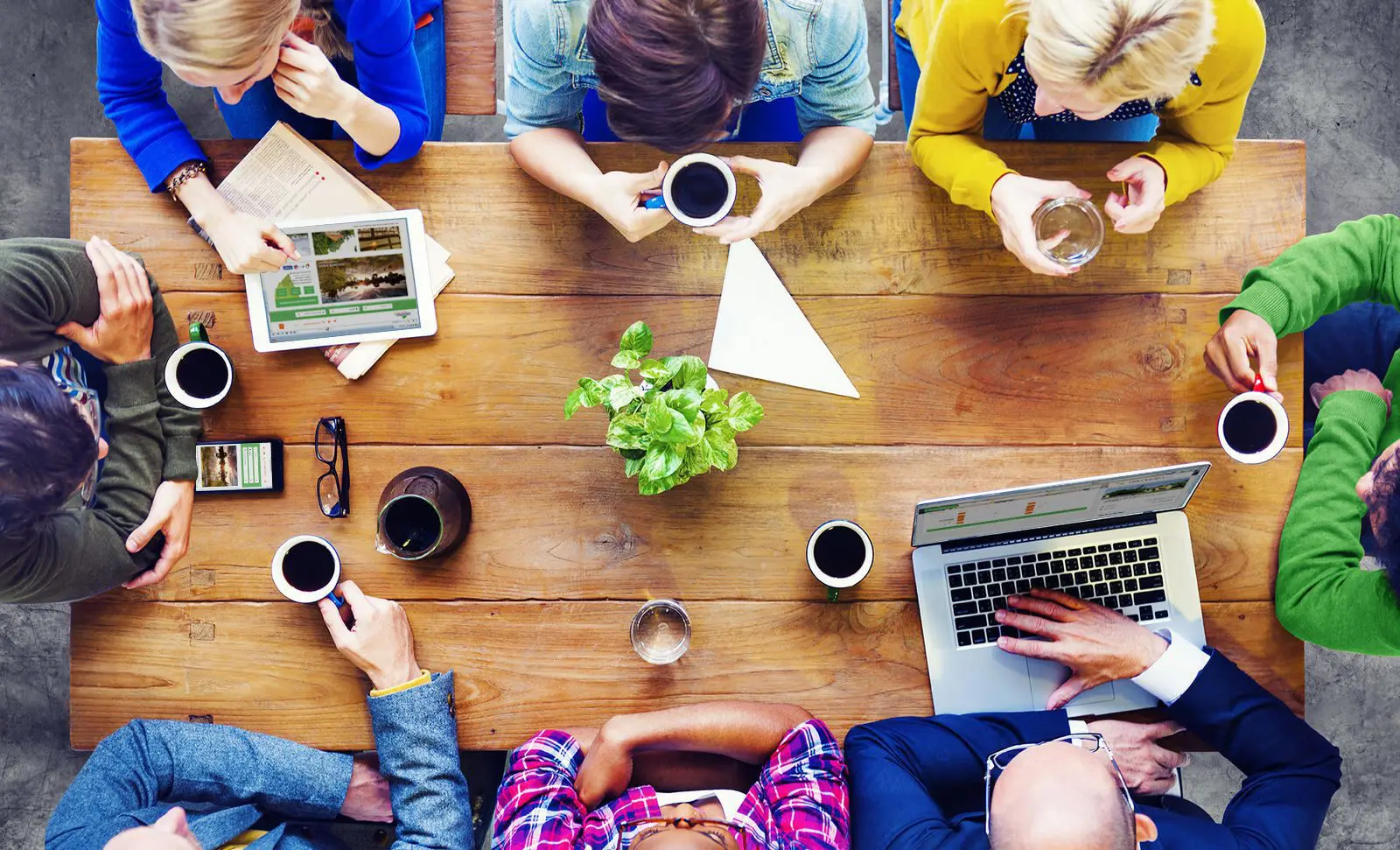 Gruppe von Menschen bei einer Besprechung am Tisch mit Laptop und Kaffee.