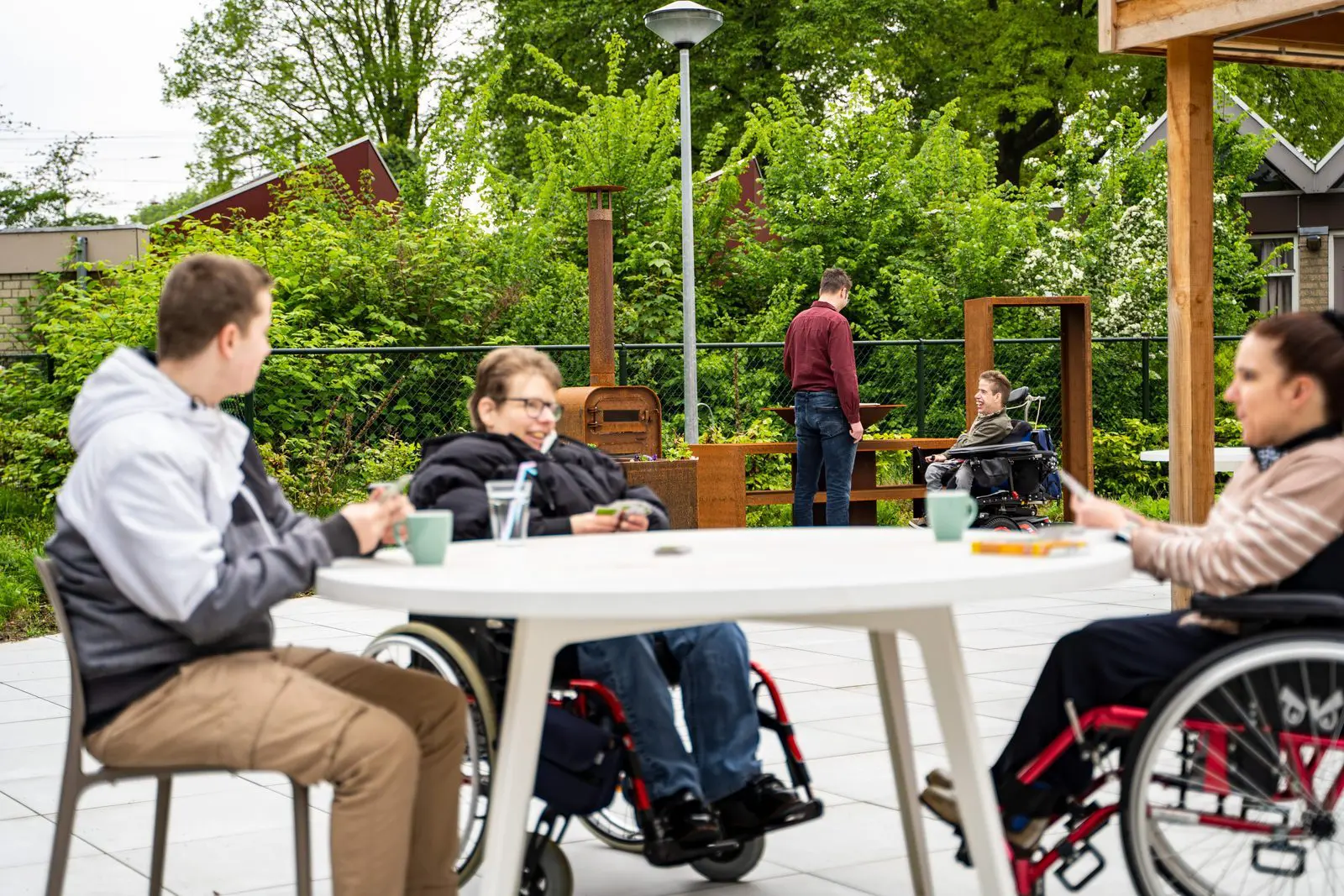 Menschen im Rollstuhl sitzen gemeinsam auf einer Terrasse einer barrierefreien Gruppenunterkunft.
